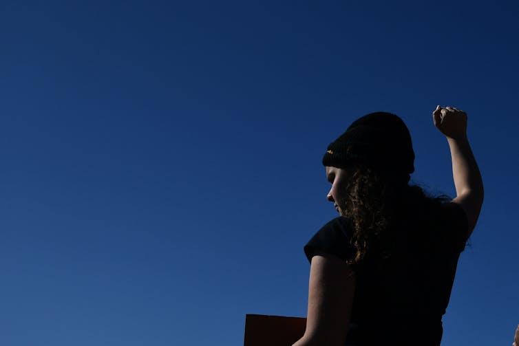 Young Indigenous woman holds her fist to the sky.