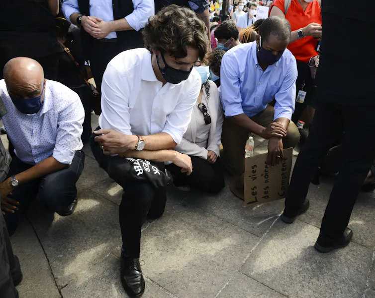 Justin Trudeau, in a mask, kneels on one knee.