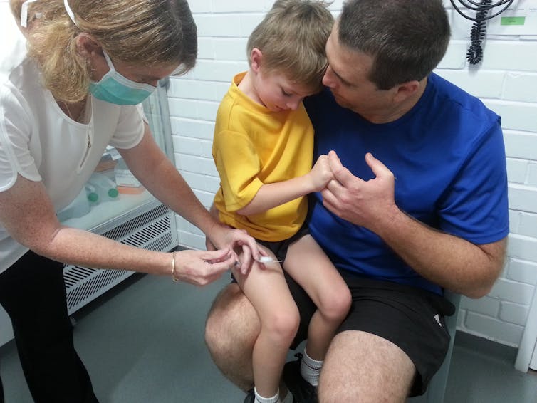 The author's son having his four-year-old vaccinations. He's sitting on his father's knee and receiving it in his thigh.