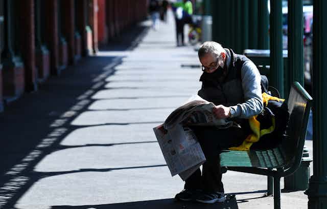 Man on bench reading newspaper 