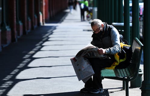 Man on bench reading newspaper