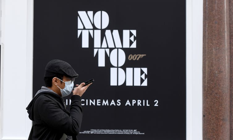 Face-masked person walks past poster for James Bond with the words No Time To Die and