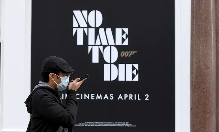 Face-masked person walks past poster for James Bond with the words No Time To Die and
