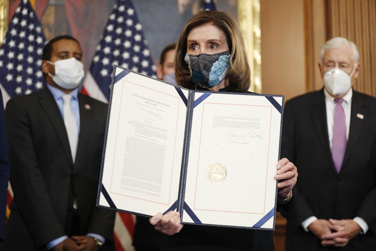 Nancy Pelosi wearing a COVID mask and holding up a folder containing the Article of Impeachment against Donald Trump, January 13 2021.