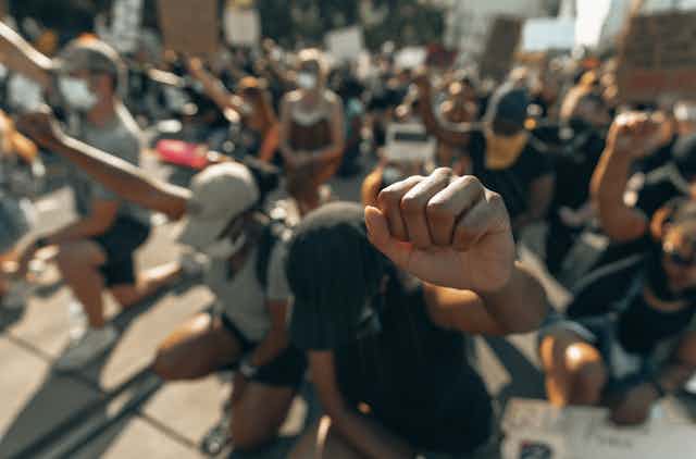 This image shows a close up a fist. All people in the photo are kneeling with raised fists. 