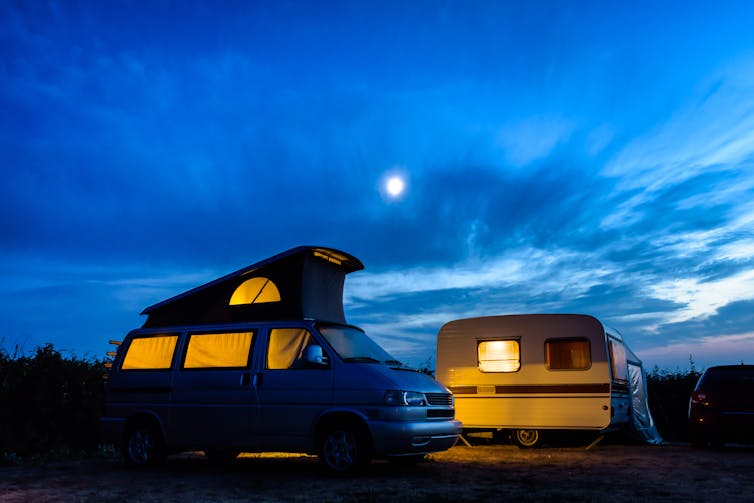 A caravan and camper van lit up at dusk.