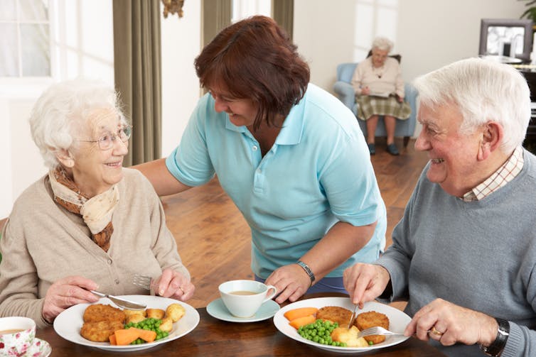 A woman chats with an elderly couple siting at a table having a meal