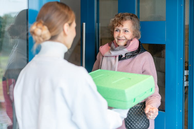 A woman hands a container to an elderly woman.