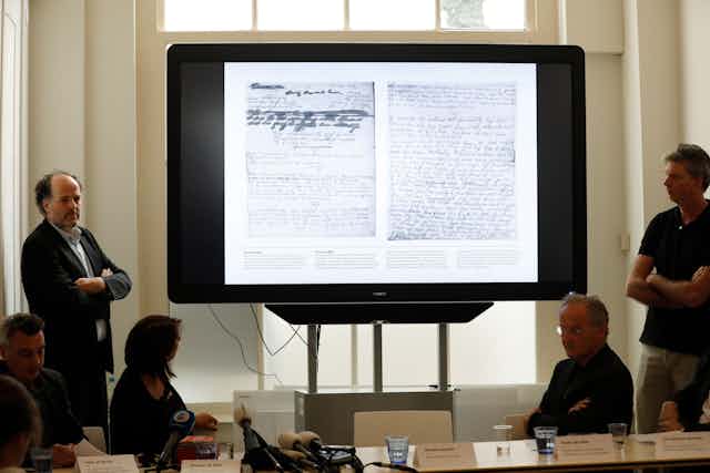 Handwritten pages are shown on a screen during a meeting.