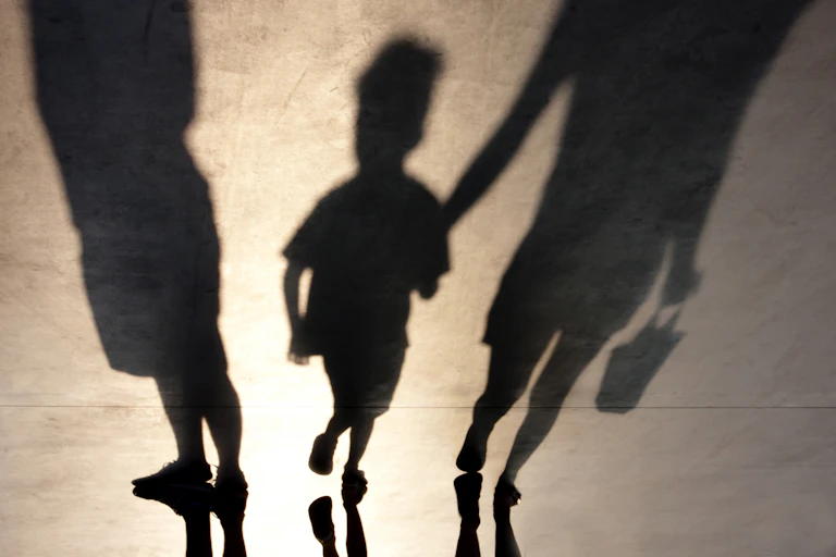 Sombras de dos adultos y un menor de la mano de uno de ellos.
