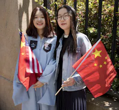two women with U.S. and China flags, one wearing a graduation gown