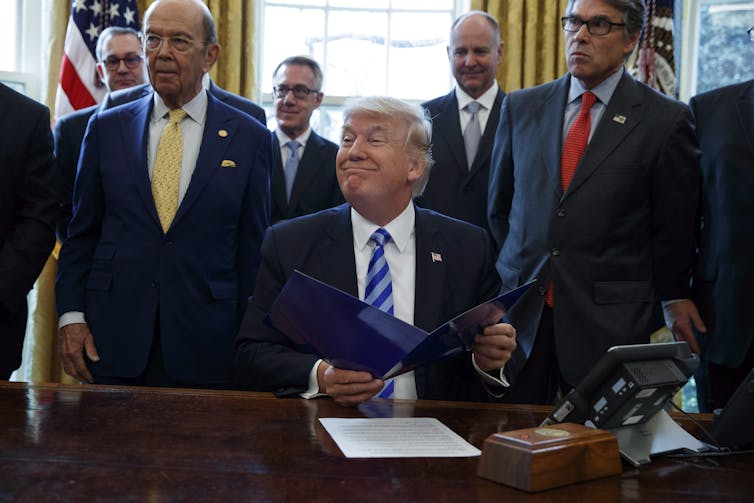Donald Trump flanked by other lawmakers in the Oval Office of the White House.