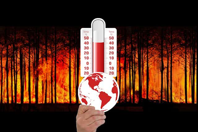 Tangan memegang globe dan termometer dengan latar belakan gambar hutan terbakar.