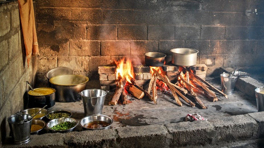 Wood fire burning on a brick hearth, with pots and dishes containing food nearby