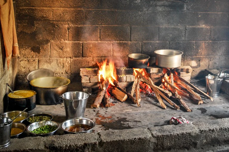 Wood fire burning on a brick hearth, with pots and dishes containing food nearby
