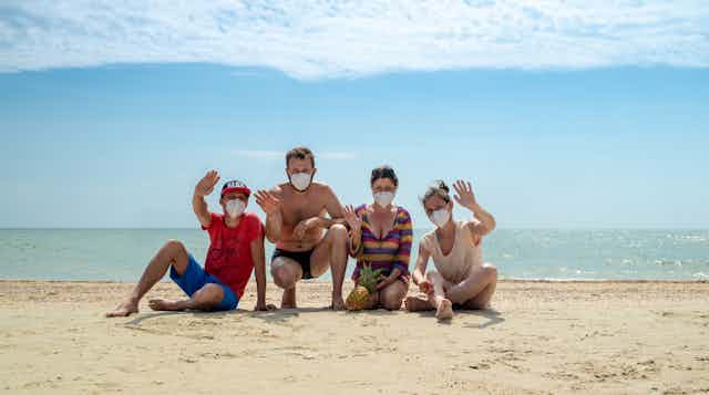 Two men and two women in face masks pose for photo on the beach