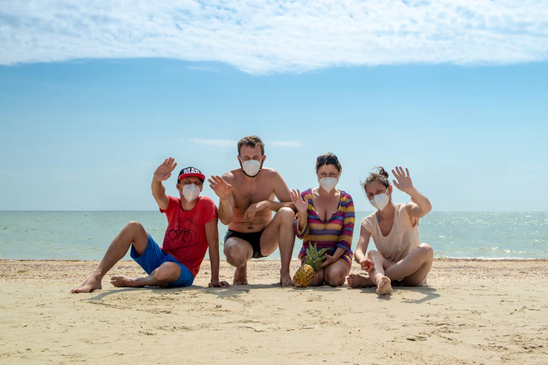 Two men and two women in face masks pose for photo on the beach