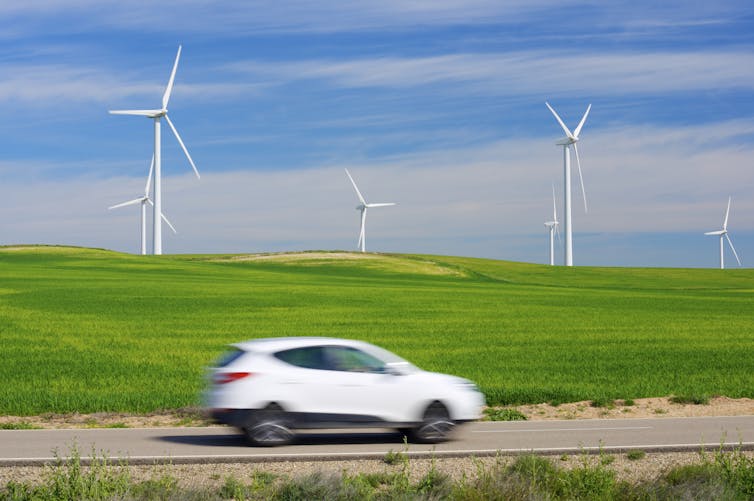A car drives past a field with wind turbines