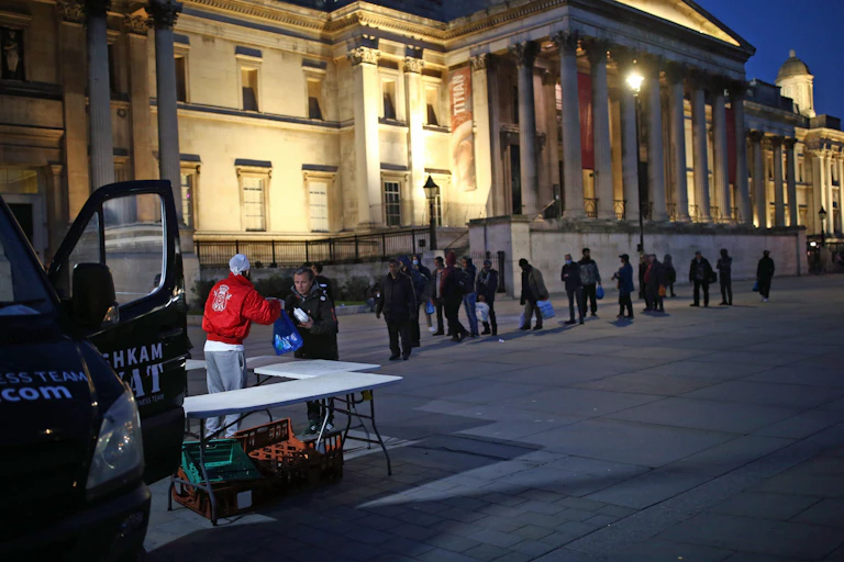 People queue up to receive food from a charity van in London.