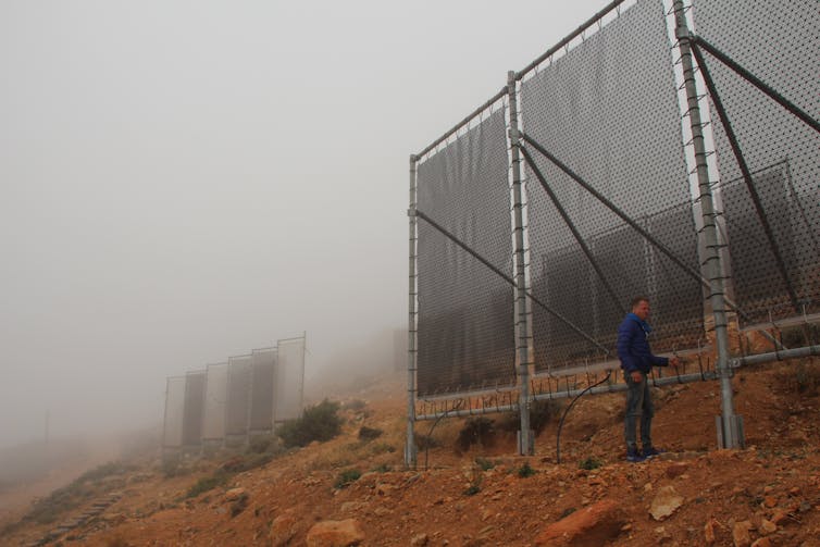 Large nets erected vertically on hillside covered in fog.