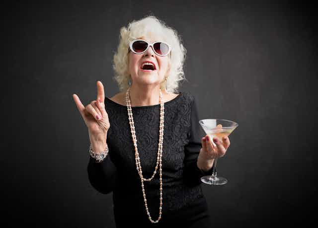 Grandma with glasses and drink in hand showing rock sign