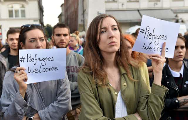 Two women holding up signs that say “#Refugees welcome” at a protest in Poland 