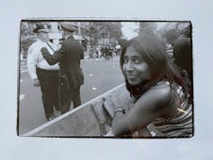A woman stands at a police barrier on the street. Two white police offers in the background.