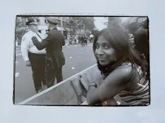 A woman stands at a police barrier on the street. Two white police offers in the background.