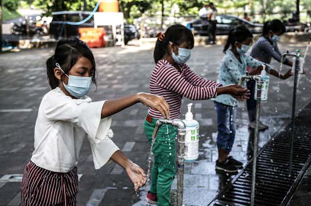 Four children wash their hands at outdoor handwashing stations