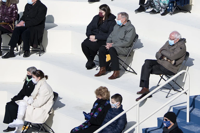 People sitting on folding chairs in pairs, six feet apart.