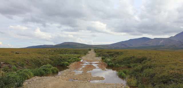 A road with puddles and clouds in the arctic tundra