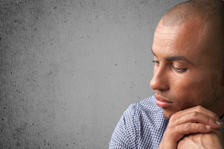 Profile of a pensive man with his cheek resting on his clutched hands