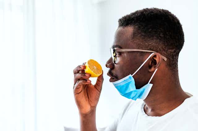 A man sniffs an orange with his medical mask down.