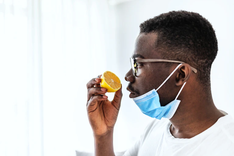 A man sniffs an orange with his medical mask down.