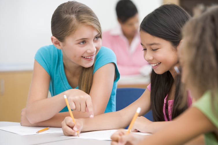 Three girls at school talking at the desk.