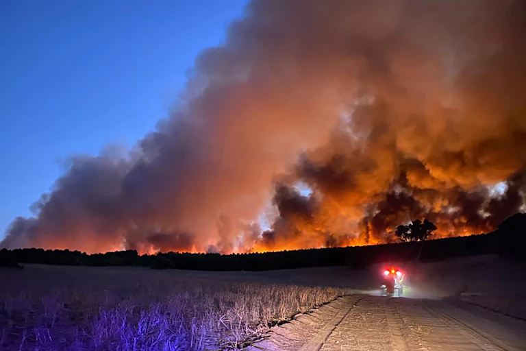 Smoke billows from an orange horizon at the end of a dirt road.
