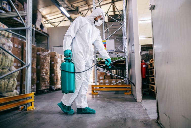 Man in a protective suit and mask disinfecting warehouse full of food products.