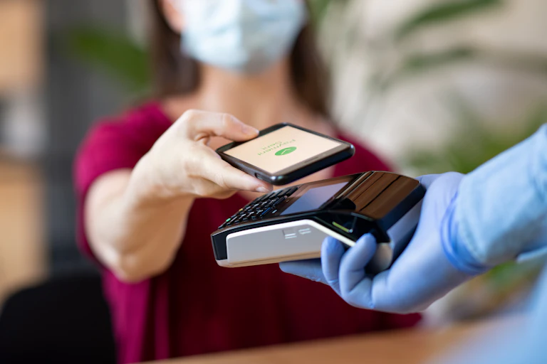 A masked woman makes a contactless payment with her phone
