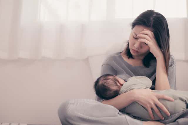 A tired and sad-looking mother breastfeeds her child.