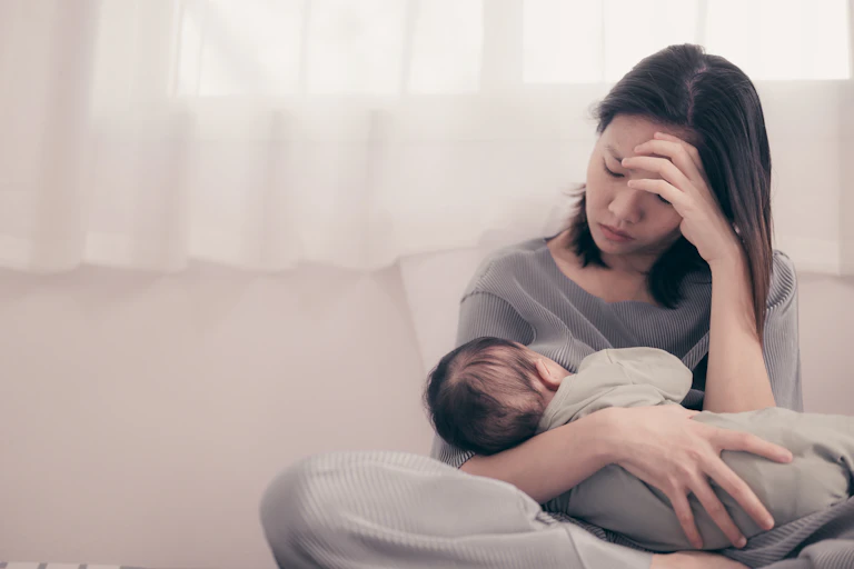 A tired and sad-looking mother breastfeeds her child.