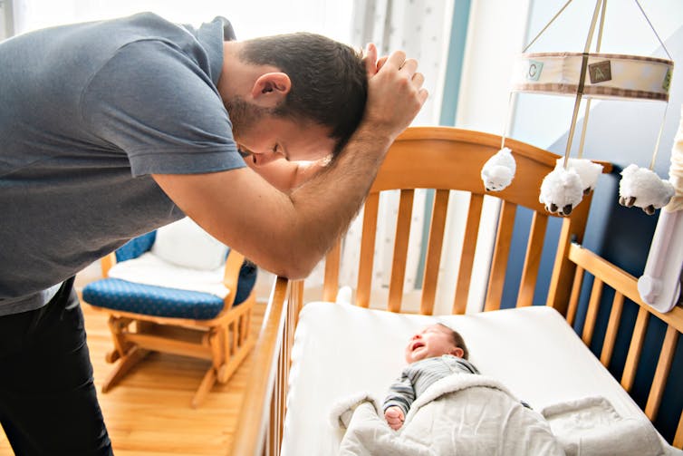 New father bends over crib looking exhausted.