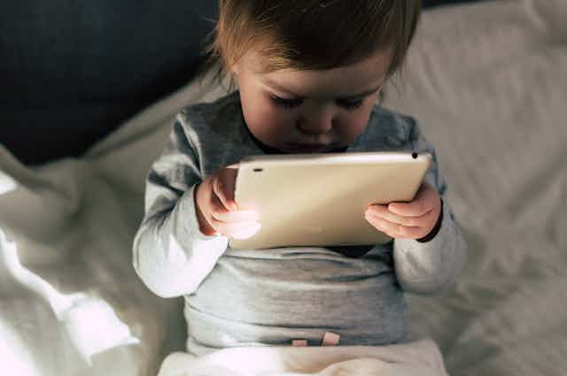 A toddler holds a touchscreen tablet close to their face