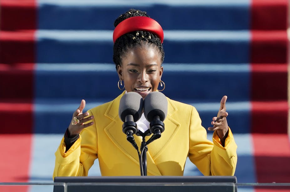 An African American woman wearing a yellow coat reads a poem.