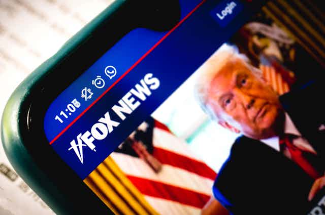A close-up of a smartphone shows a Fox News article accompanied by an image of Donald Trump.