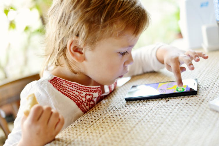 A young girl uses a touchscreen phone on a kitchen table