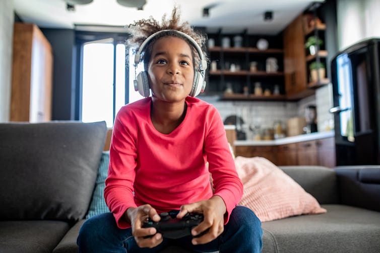 A lively engaged girl sits on a couch playing video games.