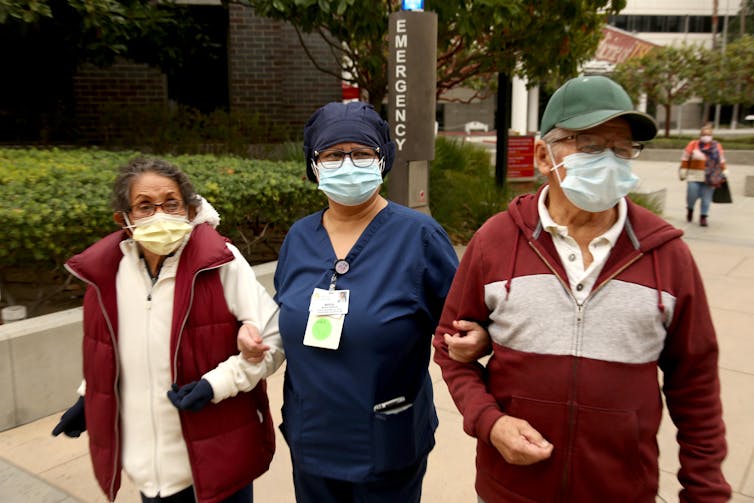 Health care worker holds arms of elderly man and woman