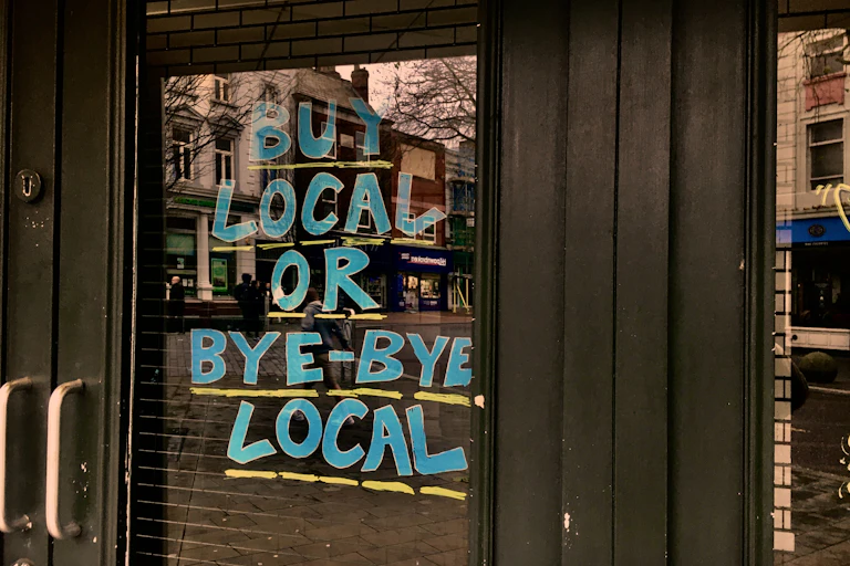 A storefront with a sign that reads Buy Local or Bye-Bye Local.