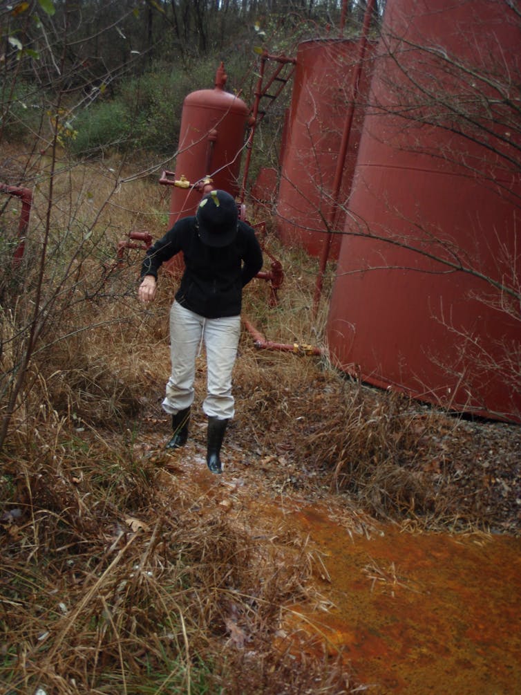 A woman walks through an oil spill near tanks.