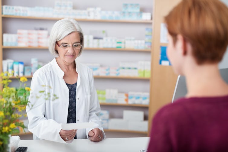 A pharmacist studies a woman's prescription.